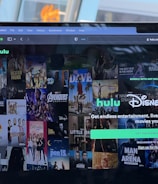 A laptop screen displays a web page featuring a mix of movie and TV show covers, highlighting popular titles and a Hulu and Disney+ bundle promotion. There are visible icons and images of films and shows alongside promotional text offering entertainment and live sports.
